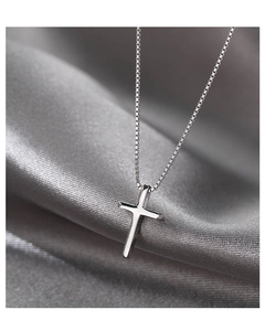 Detail view of a polished silver cross pendant on a box chain over dark silk fabric