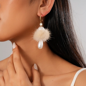 Detail of elegant beige pompom and teardrop pearl earring worn by a model
