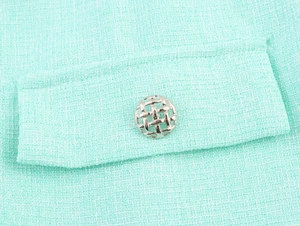 Close-up of light green tweed fabric texture and ornate silver metal button detail