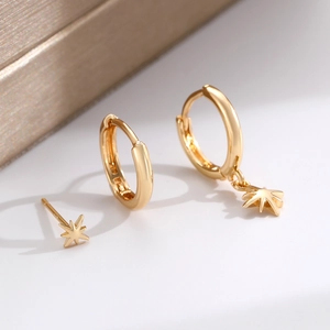 Macro shot of gold starburst stud earring and hoops set on a white surface with gift box