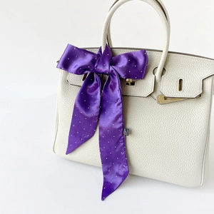 Eleganter lila Satinschal mit silbernen Punkten, an einer weißen Handtasche verknotet