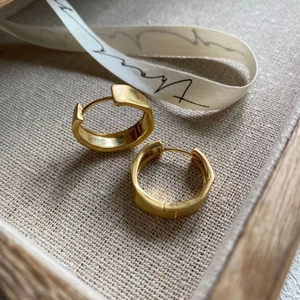 Detail of chunky gold hoop earrings with a brushed finish on a natural textured fabric