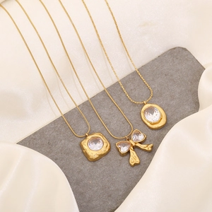 Gold stainless steel butterfly and geometric diamond pendant necklaces on stone background