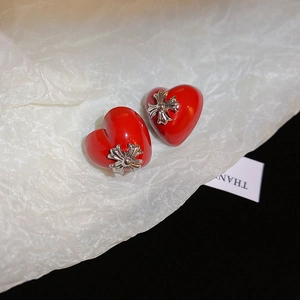 Macro shot of red heart earring with silver cross detail on textured background