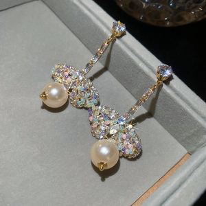 Detail of gold butterfly earrings with colorful zircons and hanging round pearls