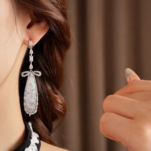 Close-up of silver drop earrings with bow design and zircon stones worn by a model