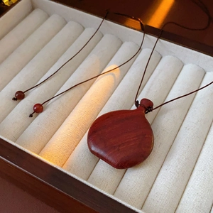 Close-up of a wood gourd pendant necklace on velvet display with red bead accents