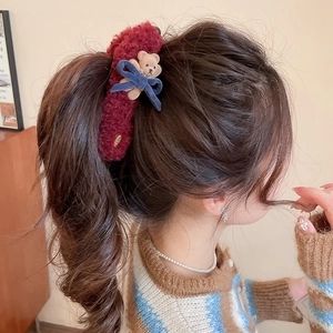 Detail of cute plush bear hair clip with blue bow worn on a stylish ponytail hairstyle