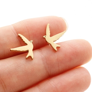 Detail shot of golden bird stud earrings held on fingertips showing realistic scale