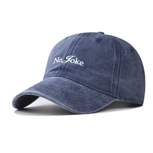 Detail view of white NO JOKE embroidery on a vintage washed navy cotton baseball cap