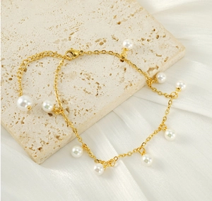 Detailed shot of 18K gold tassels and white pearls on a minimalist stainless steel anklet
