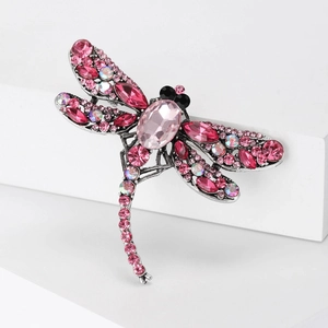 Detail view of silver insect brooch featuring pink and iridescent crystals on white background