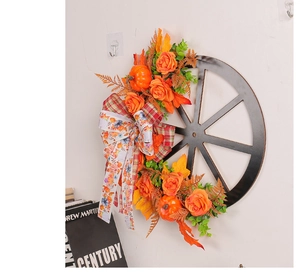 Detail of autumn wreath with orange roses, mini pumpkins and a plaid bow on a black wheel