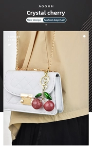 Close-up of sparkling red crystal cherry charm with gold leaf hanging on a luxury white handbag