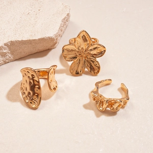 Detail of three gold irregular flower and lava textured rings on a beige stone background