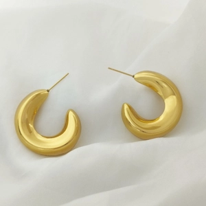 Macro view of gold minimalist C-shaped hoop earrings on elegant white fabric