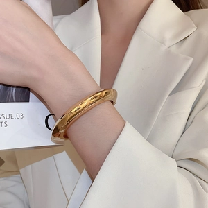 Detailed view of chunky golden oval cuff bracelet with mirror-polished metallic surface
