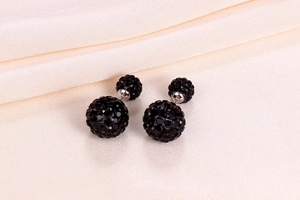 Macro detail of double-sided black crystal ball earrings on soft beige fabric