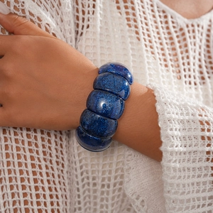 Detail view of chunky blue acrylic stretch bracelet with glitter on model's wrist