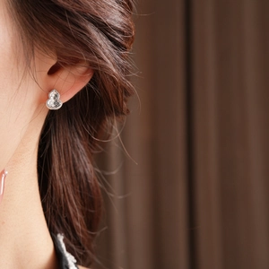 Close-up of silver gourd-shaped stud earring with textured surface on a model's ear