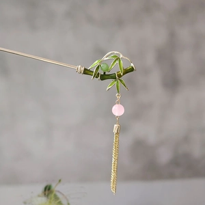 Detailed macro view of a bamboo style green hair stick with pink beads and golden tassels