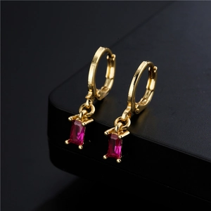 Golden earrings with rectangular red zircon pendant on a black reflective background