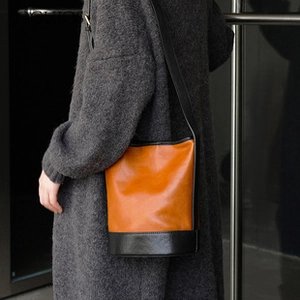 Detail view of a two-tone leather bucket bag in orange and black worn by a model