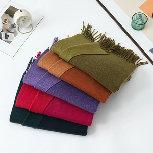 Folded fringed scarves in olive, caramel, purple, red, and teal on a cozy setup