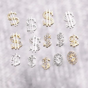 Close-up of gold and silver dollar sign nail charms with shimmering rhinestone inlay