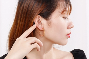 Close-up of a gold beaded hoop earring worn by a model, showing texture and size