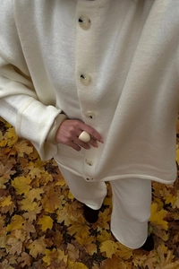 Detail of beige knit cardigan set with buttons and trousers on golden autumn leaves