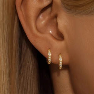 Close-up of golden hoop earrings featuring marquise-cut zircons worn on ear