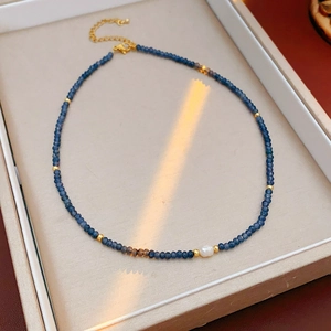 Detail showing blue beaded necklace with a central white pearl and gold clasp hardware