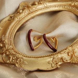 Elegant gold-tone heart earrings with deep red enamel inlay on vintage satin background