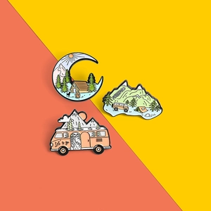 Detail of three outdoor adventure enamel pins featuring mountains, forests and a retro bus