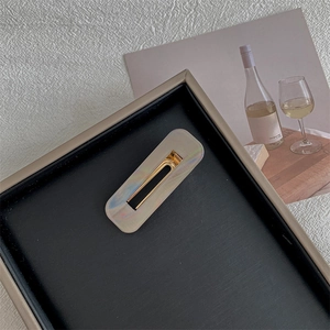 Close-up of rectangular iridescent hair clips on a black textured tray for styling