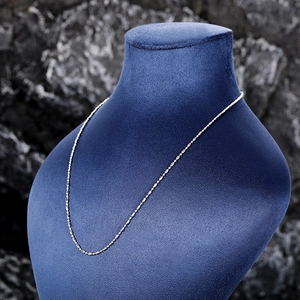 Detail view of silver chain necklace on a blue velvet mannequin against a dark rock background