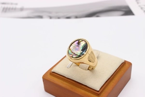 Macro view of gold stainless steel ring with oval iridescent abalone shell on wood stand