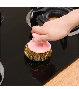 Pink handle kitchen scrub brush with steel wire ball cleaning a dark countertop surface
