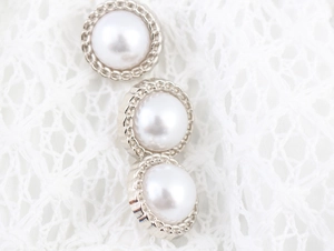 Detailed close-up of vintage pearl buttons with silver woven trim on white lace fabric