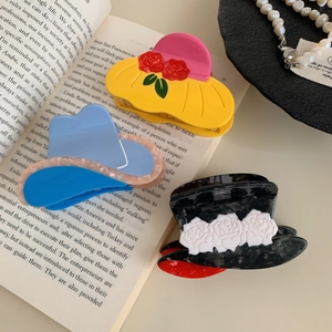 Three acetate hair claws in cowboy hat shapes with floral decor on a vintage book