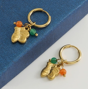 Détail de créoles dorées avec pendentifs abeilles et perles colorées sur boîte bleue
