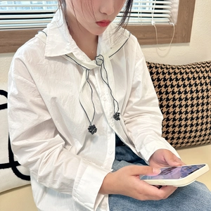 Detail of white long-sleeve blouse featuring unique tie neckline and dark contrast stitching