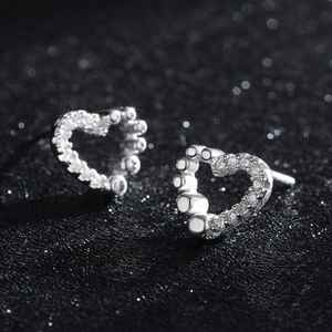 Asymmetric sterling silver heart stud earrings with shimmering zircons on black background