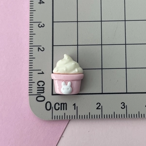 Detail view of pink resin cupcake charm with white rabbit relief on a scale mat
