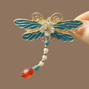 Detailed close-up of a blue enamel dragonfly hair clip with pearls and red gems