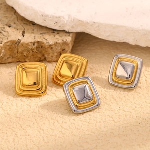 Macro di orecchini a perno quadrati in oro 18K su uno sfondo di pietra strutturata