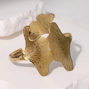 Elegante goudkleurige ginkgo blad roestvrijstalen open armband op witte stenen display