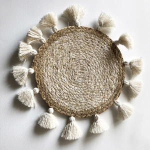 Dettaglio di decorazione murale boho in paglia intrecciata con nappe in cotone bianco