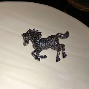 Detailed close-up of a vintage silver horse brooch with green rhinestones on ceramic